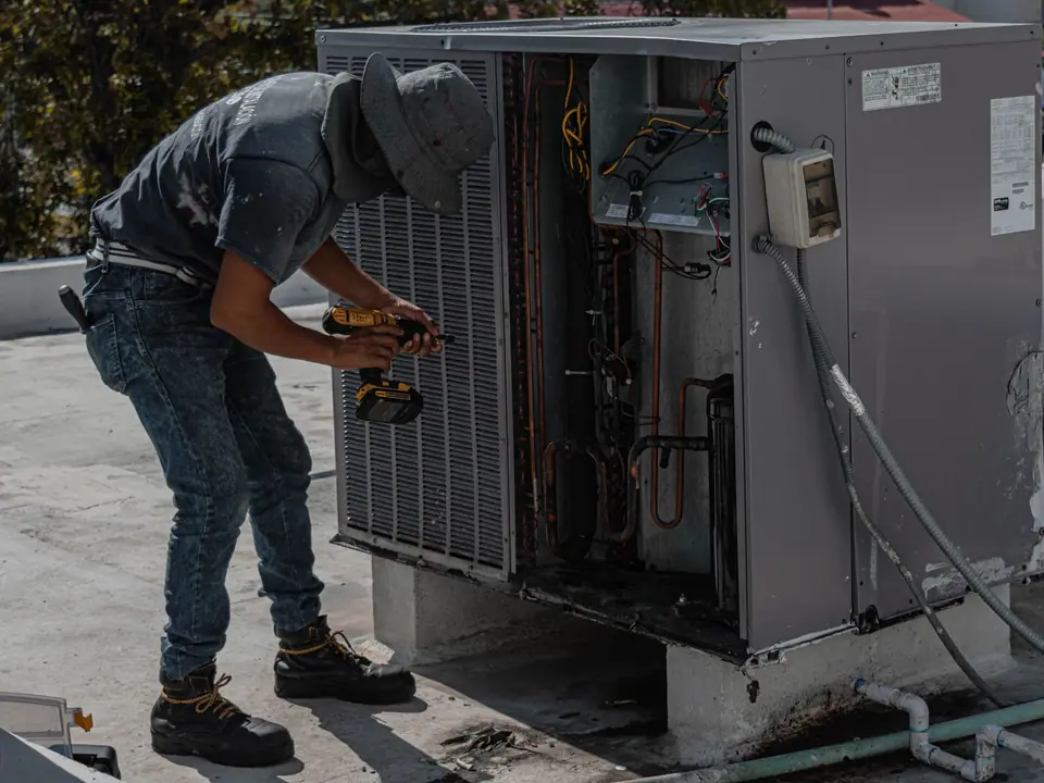 Técnico com a parafusadeira na unidade externa de um ar-condicionado, no telhado de um prédio