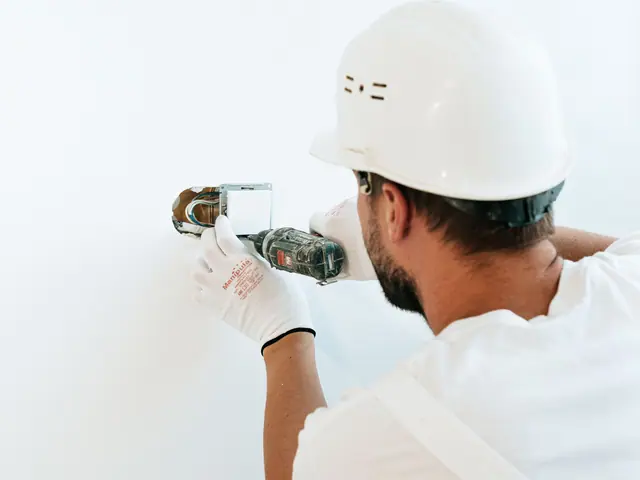 Homem de capacete e luvas usando a parafusadeira numa parede